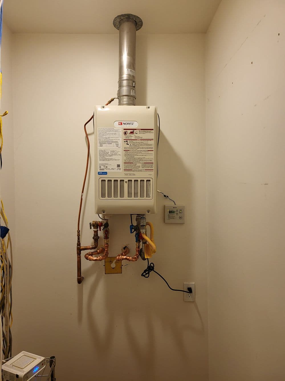 Tankless water heater mounted on a wall with copper piping and electrical connection.
