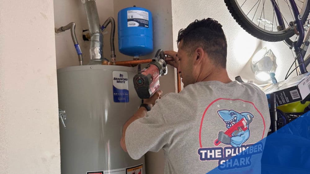Plumber repairing water heater with tools in residential garage setting.