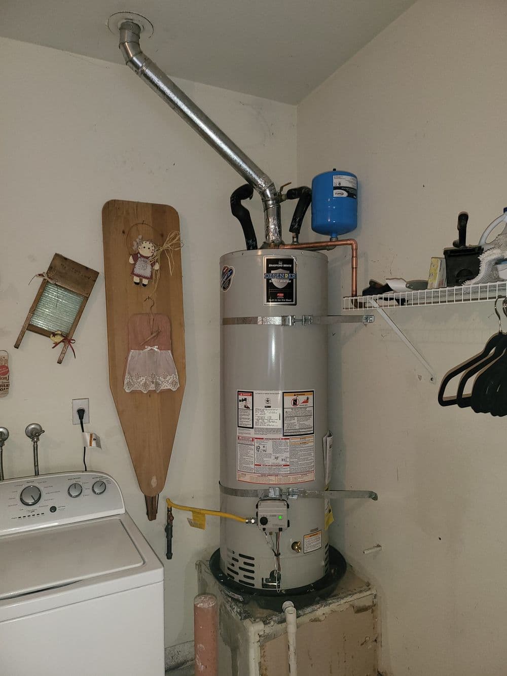 Water heater installed in laundry room with adjacent washing machine and storage shelf.