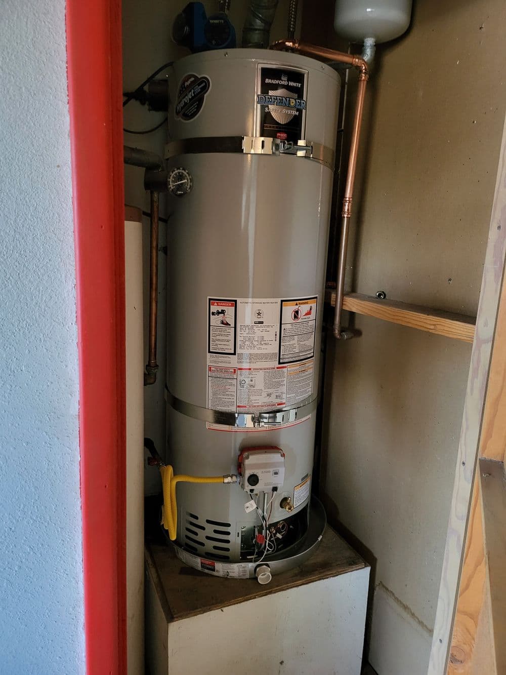 Water heater installed in a small utility room with copper piping and safety labels.