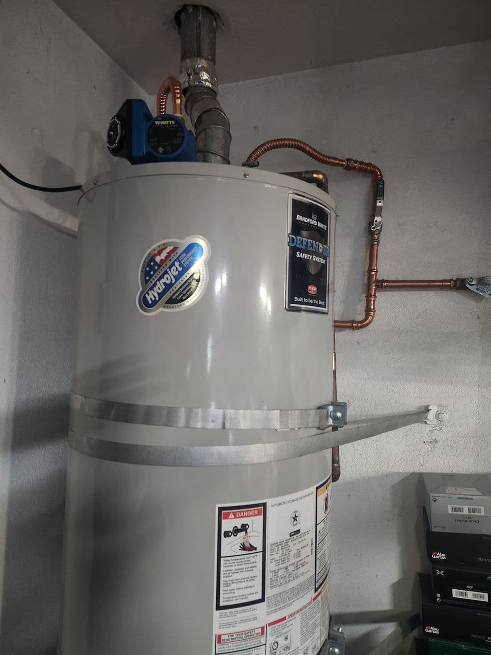 Hydronic water heater with copper piping and energy efficiency sticker in a garage setting.