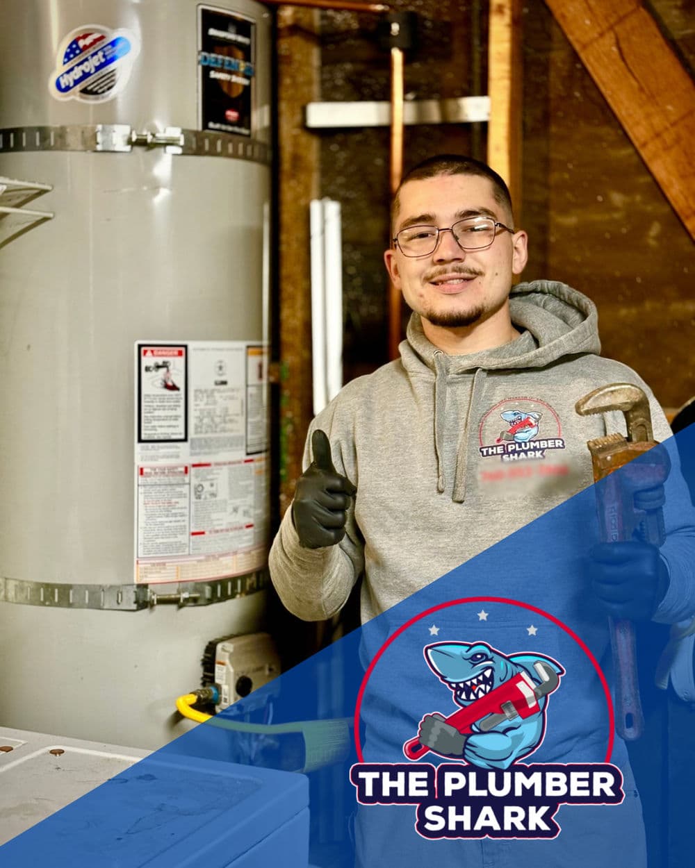 Plumber Shark technician with wrench standing next to water heater, smiling confidently.
